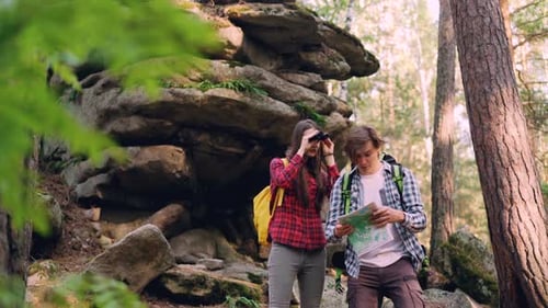 Cheerful Travelers Are Looking at Map Standing in Wood Near Rocks Discussing Way and Looking Around