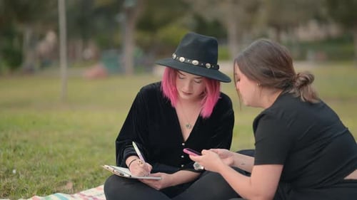 Young Women Drawing and Using Phone in Park