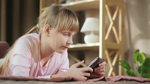 Side View of Child Rests in His Room, Uses a Smartphone