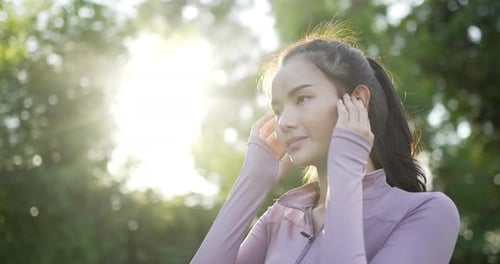 Woman in sportwear standing and listen music with earphone in garden