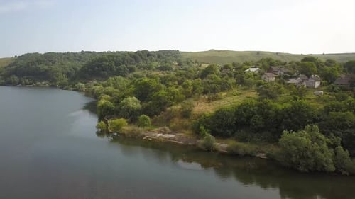 Aerial view of a small village in rural area between green trees on the shore of a big lake.