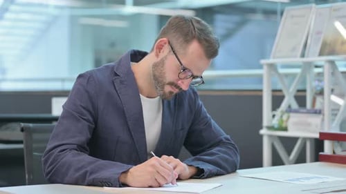 Middle Aged Businessman Writing on Paper in Office