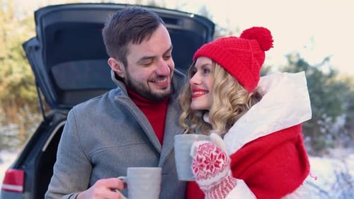 Young Couple a Man and a Woman Hugging Near the Car in a Winter and Drinking Coffee Snowy Forest