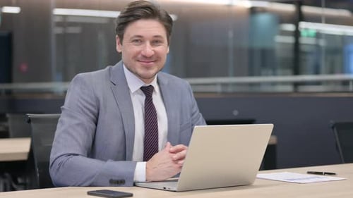 Man Smiling at Laptop in Bright Office