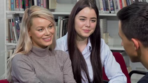 Schöne College-Mädchen lachen und sprechen mit ihrer Klassenkameradin in der Campus-Bibliothek