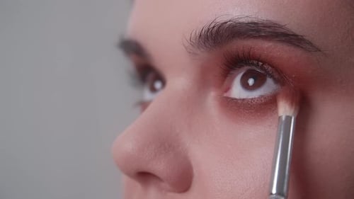 Une maquilleuse applique un eye-liner rose sur un œil féminin avec un petit pinceau