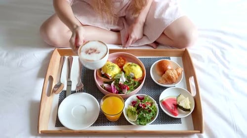 Woman Hand Puts a Cup of Coffee Breakfast in Bed Served in Hotel Room