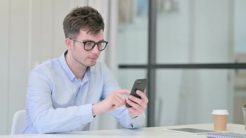 Joven atractivo usando un teléfono inteligente en la oficina