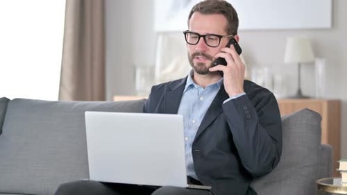Man Answers Cell Phone While Using Laptop At Home