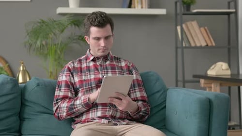 Young Man Using Tablet on Couch Indoors