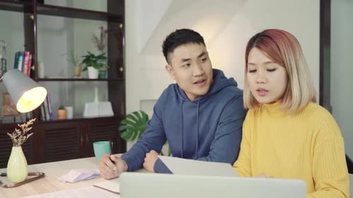 Young couple managing finances, reviewing their bank accounts using laptop and calculator at home