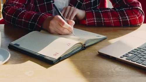 Woman Writing in Planner with Laptop on Desk