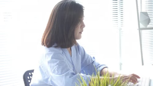 young smiling Asian woman working on laptop while at home in office work space.