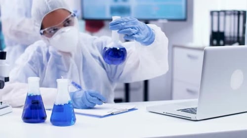 Une scientifique tapant une formule pour différents fluides bleus fumants dans un laboratoire de chimie