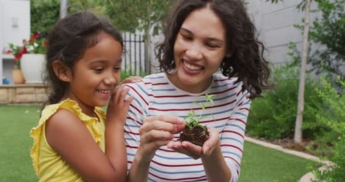 Hispanic mother and daughter teaching planting flowers in the garden
