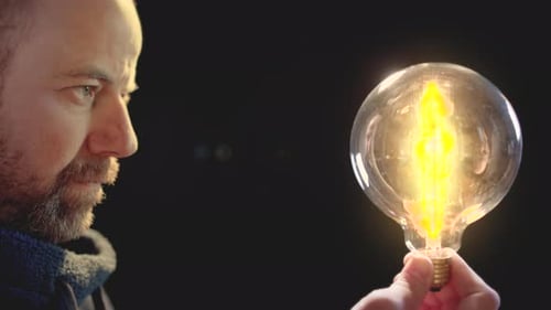 Man holding light bulb against black background that loses energy. Concept of global energy crisis