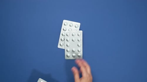 Hand Places Pill Blister Packs on Blue Surface