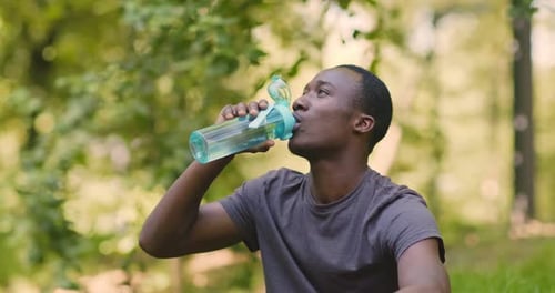 African American Guy Drinking Water, Resting in Park After Run Workout