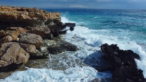 Sea Washes the Rocky Shore Above Aerial Shot Flying Over Coastline Cliffside with Blue Pure Water