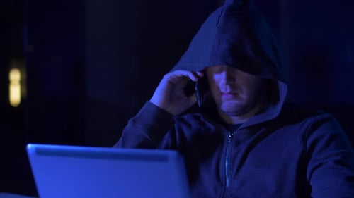 Hooded Figure Using Laptop and Cell Phone