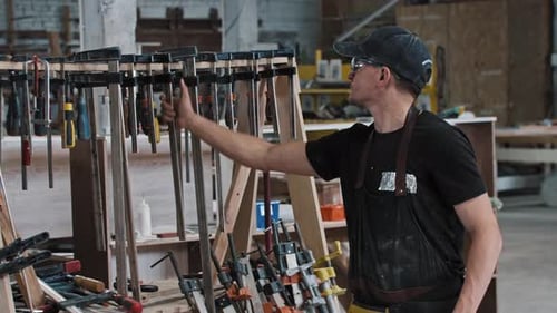 Man in a Carpentry Workshop Takes an Instrument Looking in the Camera