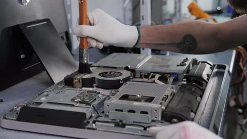 Nahaufnahme von männlichen Händen, die mit einer Bürste an der Demontage und Reinigung der Leiterplatte im Laptop arbeiten