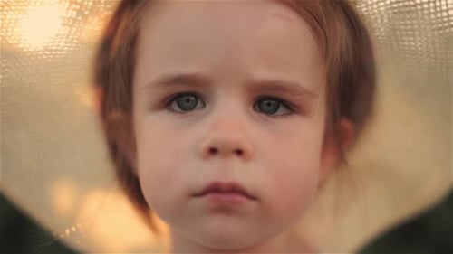 Serious Sad Little Girl with Hat Looking at Camera While Standing in a Park on a Cloudy Summer Day