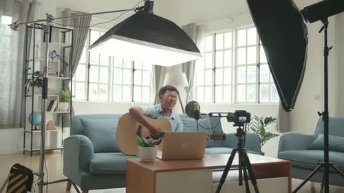 Niño asiático tocando la guitarra y cantando una canción mientras transmite. Equipo de iluminación profesional