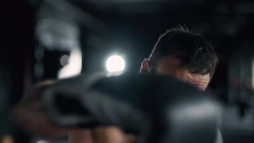 A Muscular Sportsman is Boxing in the Dark Gym