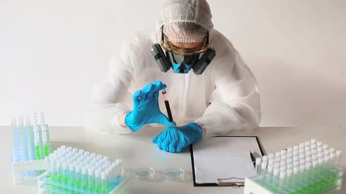 Arzt in einem weißen Schutzoverall und Atemschutzgerät beim Betrachten einer Blutprobe in einem Reagenzglas und