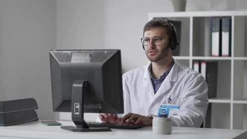 Médico general masculino con bata blanca sentado en el escritorio en el consultorio del médico y computadora de desplazamiento