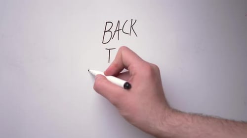 The hand of a young white guy is writing on a white magnetic board the words
