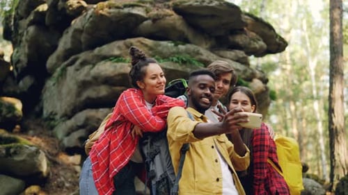 Happy African American Man Tourist Is Taking Selfie with Friends in Forest Near Huge Rocks