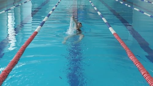 Junges Mädchen mit Brille und Mütze schwimmt im Blauwasserpool im Rückenkrawl-Strich-Stil