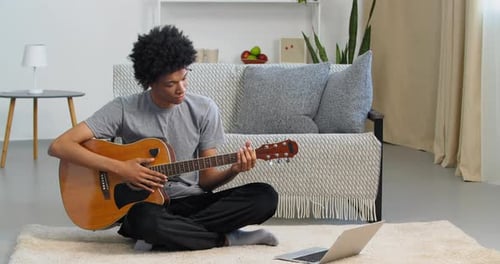 Young Adult Plays Guitar While Using Laptop
