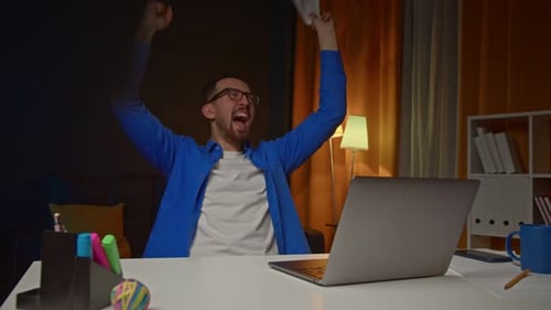Man Celebrates Success at Desk in Warm Light