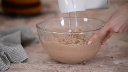 Professional confectioner whipping chocolate cream using a handheld electric mixer.