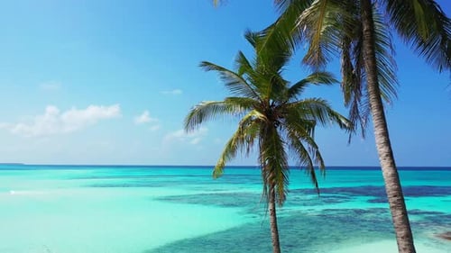 Daytime flying travel shot of a white sand paradise beach and blue ocean background in colourful 4K