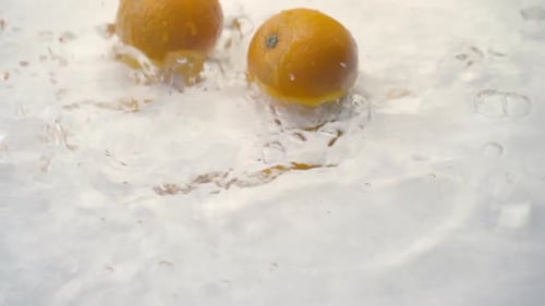 SLOMO of Oranges Falling into Water on White Backdrop