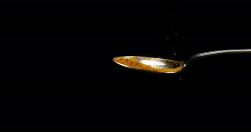 Spoon and Curry Powder falling against Black Background, Slow motion 4K