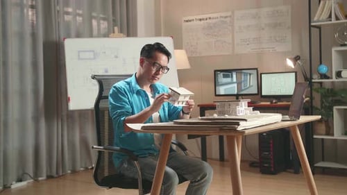 Asian Man Engineer With A Laptop Making Paper Model Of House At The Office