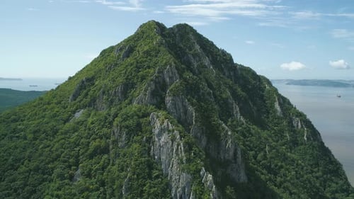 Aerial View of the Tall Mountain Covered By the Forest Towering Over the Empty Valley and Sea on