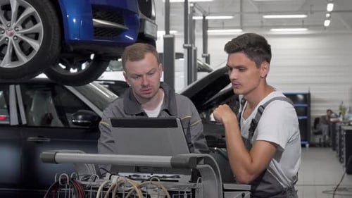 Dos mecánicos de automóviles hablando en el garaje usando una computadora portátil en el diagnóstico del automóvil