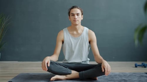 Slow Motion Portrait of Male Yoga Instructor Sitting on Mat in Nice Studio and Looking at Camera