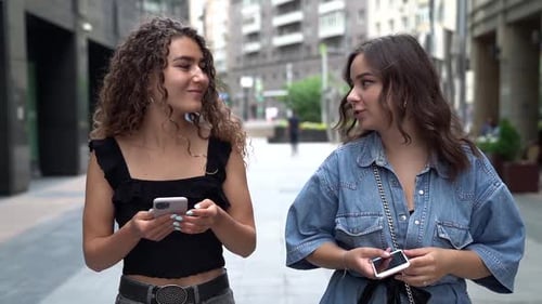 Two Young Female Friends Are Walking Together on City Street at Summertime