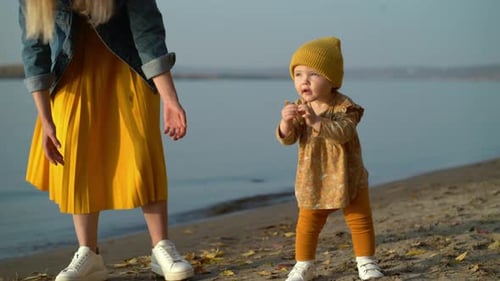 Mama hält ihre Tochter an der Hand und bringt ihr bei, am Strand zu laufen
