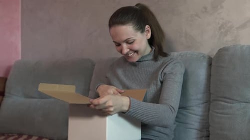 Young Woman Opens a Delivery Box at Home