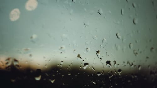 Raindrops Streaking Down a Window During Sunrise