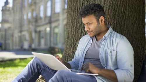 Young Adult Studies with Laptop Outdoors on Campus