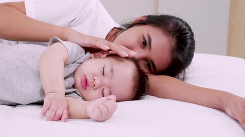 Loving Mother Resting with Sleeping Baby on Bed